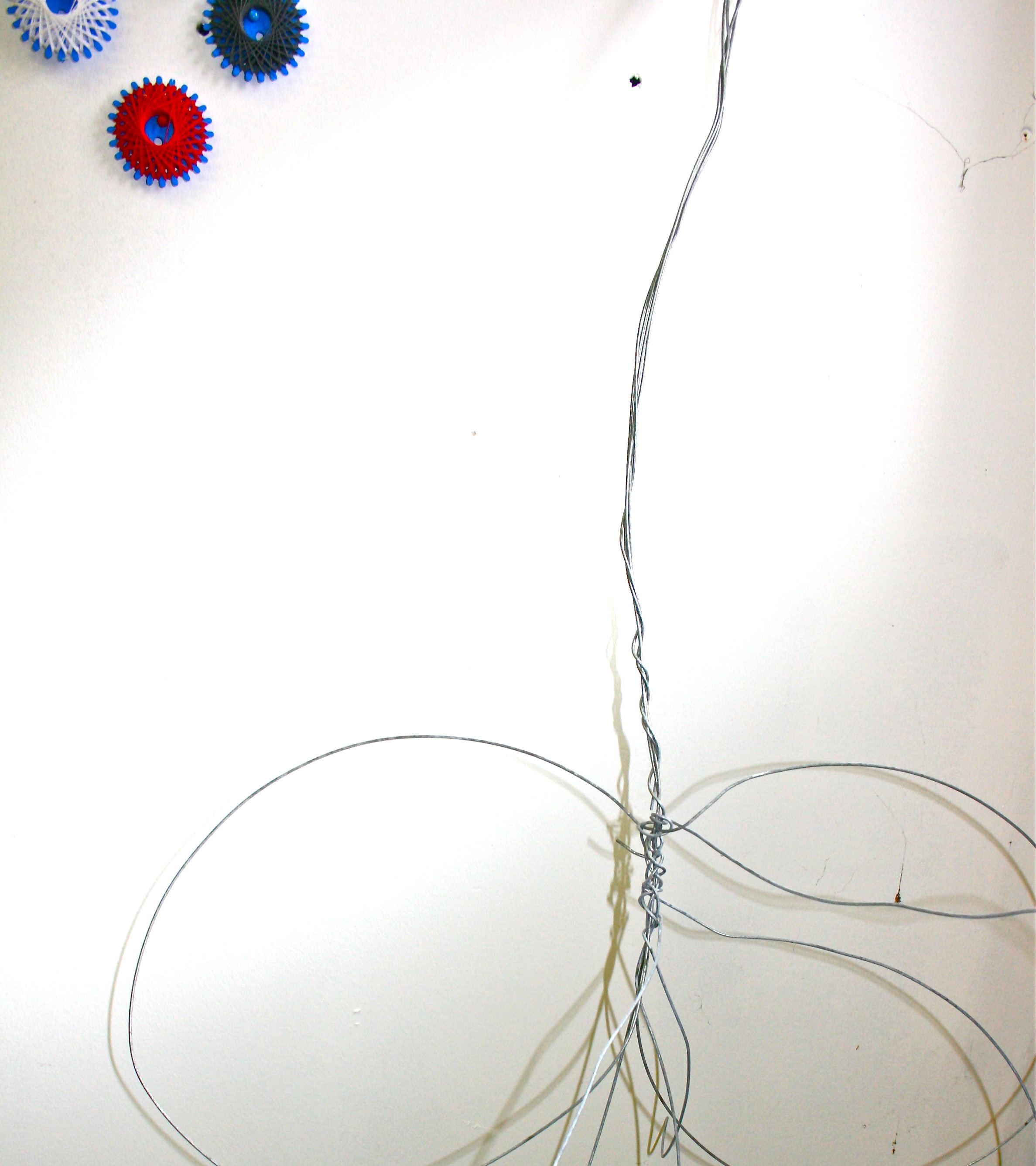 Geometric threads, intertwining wire strands weave together winding up towards the top of image with 3 geometric reels with black, white and red threads