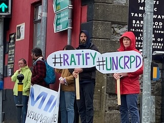 Ratify the UNCRPD People holding signs with hashtags #RATIFY and #UNCRPD during a street protest