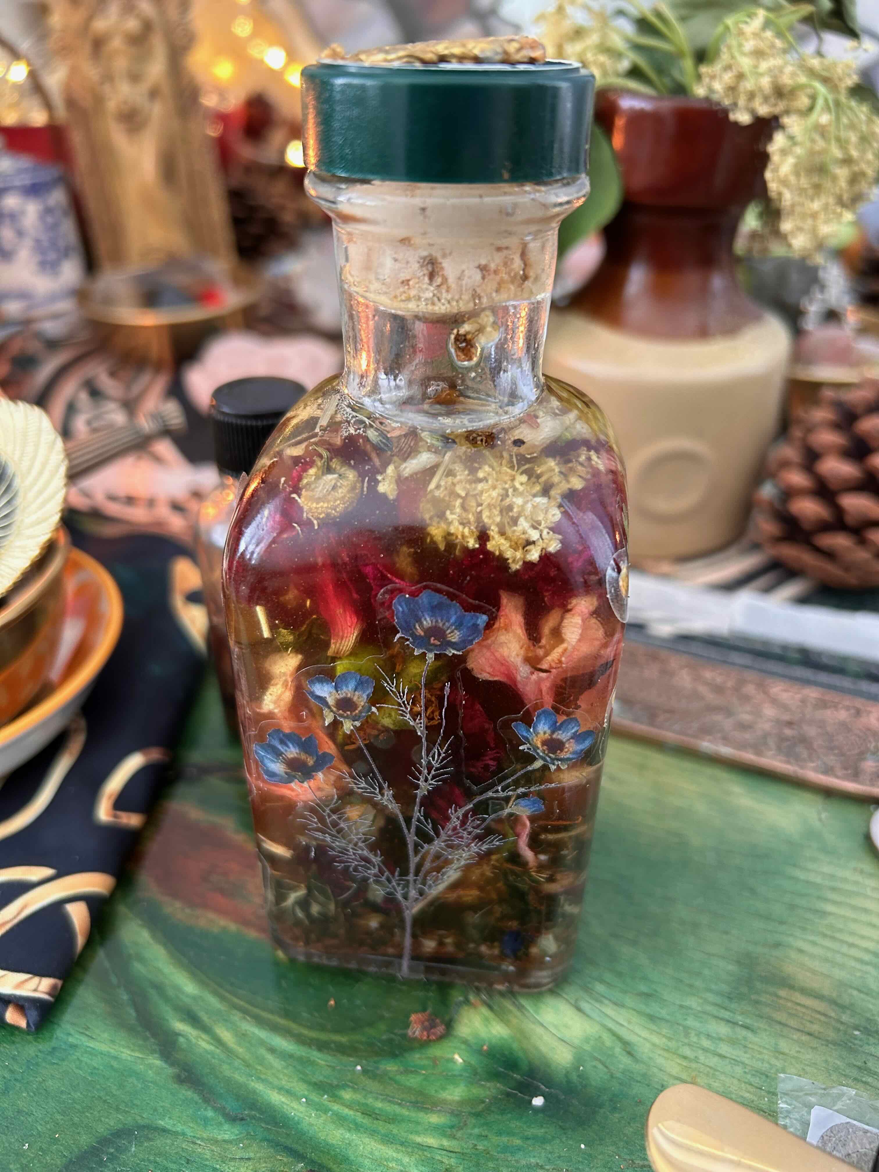 Glass bottle with dried flowers and herbs preserved inside, sealed with a green cap, on a green wooden surface