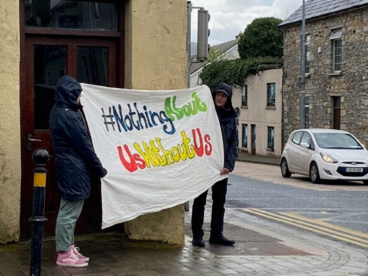 Nothing About Us without Us Two people holding a banner that reads '#NothingAboutUsWithoutUs' on a street corner
